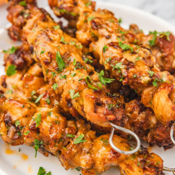 bang bang chicken skewers stacked on a plate.