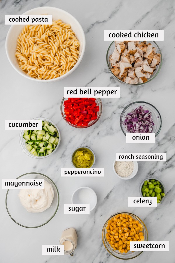 ingredients to make pasta salad with chicken laid on a white marble surface.